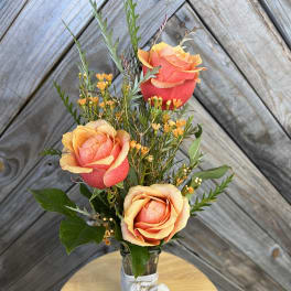 Three coral roses in a small glass vase with a white ribbon