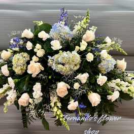 Large white and blue casket spray with roses, hydrangeas, and carnations in an elongated design