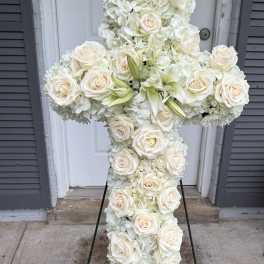 White floral cross on a metal stand with roses and lilies