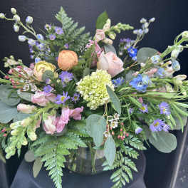Pastel garden-style flower arrangement in a clear glass vase against a dark background