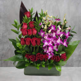 Red roses and purple orchids arranged in a rectangular vase