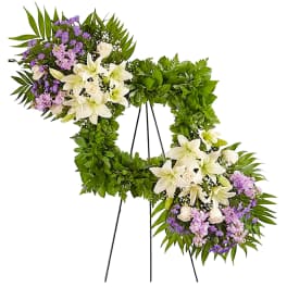 Large floral wreath on a black easel with white lilies and purple flowers