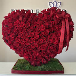 Heart-shaped arrangement of red roses on a moss-covered base with a ribbon