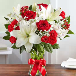 Red roses and white lilies in a glass vase with a red ribbon