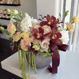Mixed bouquet of roses, orchids, and carnations in a gray vase with a burgundy ribbon