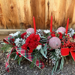 Holiday floral centerpiece with red candles, red flowers, and plaid ribbon