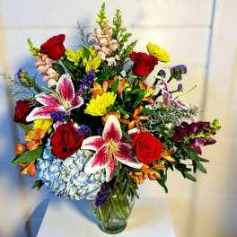Mixed bouquet of red roses, lilies, and hydrangeas in a glass vase