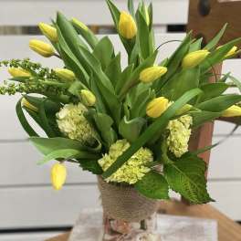 Yellow tulips and pale green hydrangeas in a glass vase wrapped with burlap