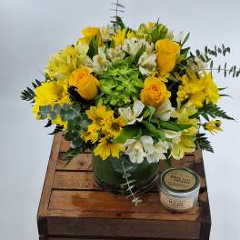 Yellow and white flower arrangement in a glass vase with a candle beside it.