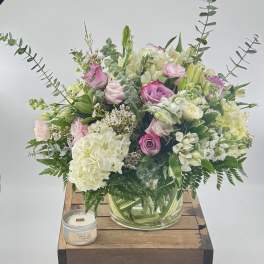 Pink and white floral arrangement in a glass vase with a candle beside it