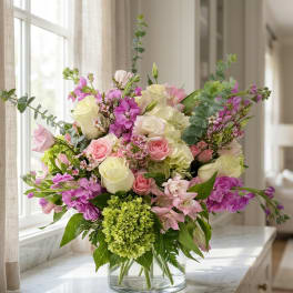 Mixed pink, white, and purple flowers arranged in a clear glass vase