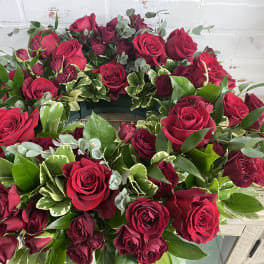 Circular wreath of red roses with mixed greenery on a white surface