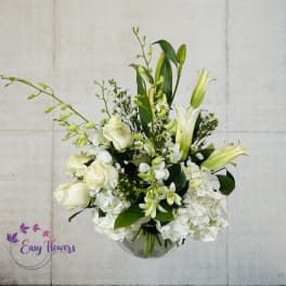 White floral arrangement with lilies, roses, and hydrangeas in a glass vase