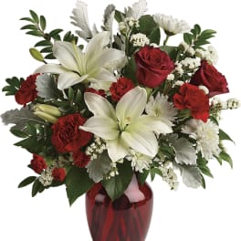Red and white arrangement with lilies, roses, and carnations in a red glass vase