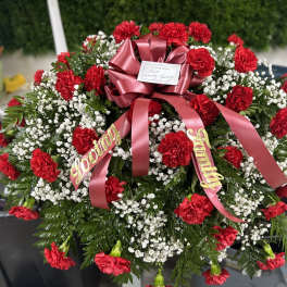 Red carnations and baby's breath arranged with a pink ribbon bow
