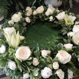 White floral wreath with roses and lilies on dense greenery