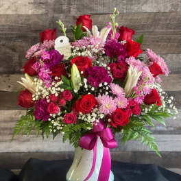 Red and pink mixed flower arrangement in a white vase with a ribbon