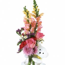 Pink and red flower arrangement with a white teddy bear in a glass vase