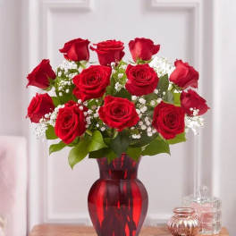 Red roses arranged in a red glass vase with white filler flowers