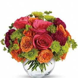Round bouquet of pink and orange roses with green mums in a clear glass vase