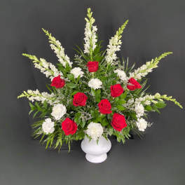 Red roses and white flowers in a white vase with greenery