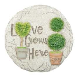 Round decorative plaque with the words "Love Grows Here" and potted topiary trees