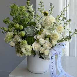 White and green floral arrangement in a white hatbox with a ribbon