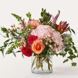 Mixed bouquet of pink, peach, and red flowers in a clear glass vase
