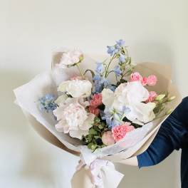 Hand-tied bouquet of pastel pink, white, and blue flowers wrapped in paper