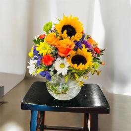 Mixed bouquet with sunflowers, orange roses, and daisies in a glass vase