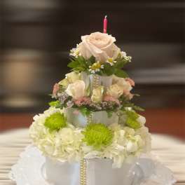 Tiered floral cake with cream roses and white hydrangeas on a doily-lined plate