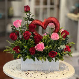 Red and pink roses arranged in a white box with a glitter heart pick