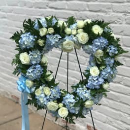 Heart-shaped floral wreath with blue hydrangeas and white roses on a stand