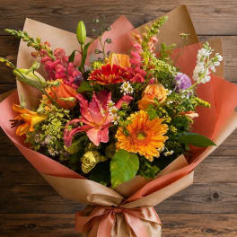 Mixed bouquet of orange, pink, and white flowers wrapped in brown paper