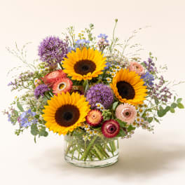 Mixed bouquet with sunflowers, purple blooms, and pink flowers in a glass vase