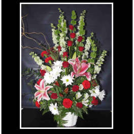 Tall mixed flower arrangement with red roses, pink lilies, and white daisies in a white vase