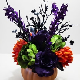 Purple, green, and orange floral arrangement in a pumpkin-shaped container