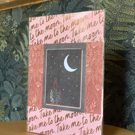 Pink greeting card with moon and stars design on a wooden surface