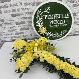 Yellow floral cross with dark green foliage on a table