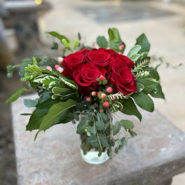 Red rose bouquet in a clear glass vase with mixed greenery
