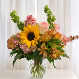 Bouquet of sunflowers, pink roses, and mixed blooms in a clear glass vase