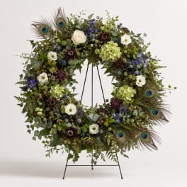Large floral wreath with white roses, blue flowers, and peacock feathers on a stand