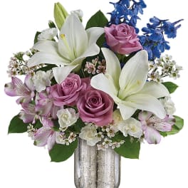 Bouquet of white lilies, pink roses, and blue flowers in a glass vase