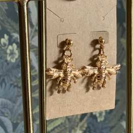 Pair of gold bee-shaped dangling earrings on a display card