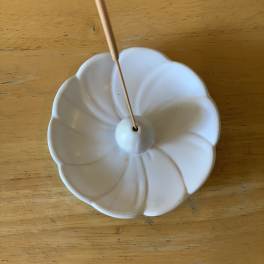 White ceramic flower-shaped incense holder on a wooden table