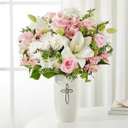 Pink and white flower arrangement in a white vase with a silver cross