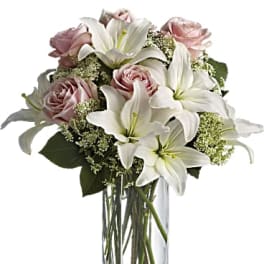 White lilies and pale pink roses in a clear glass vase