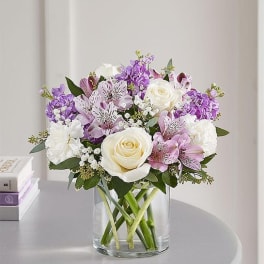 Bouquet of white roses and purple flowers in a clear glass vase