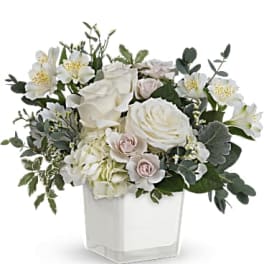 White roses and pale blooms arranged in a clear square vase