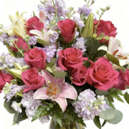 Pink roses and lilies arranged in a glass vase with lavender flowers